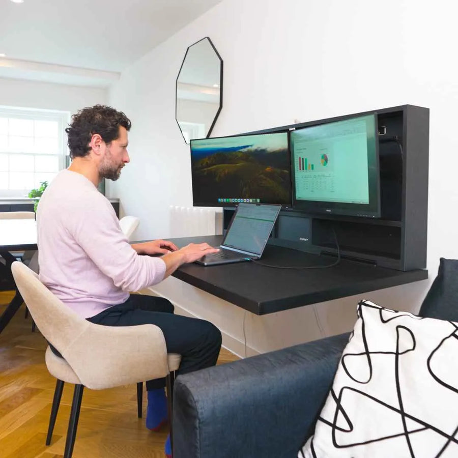 Man working at an open DropTop desk with two monitors and a laptop in a living room.