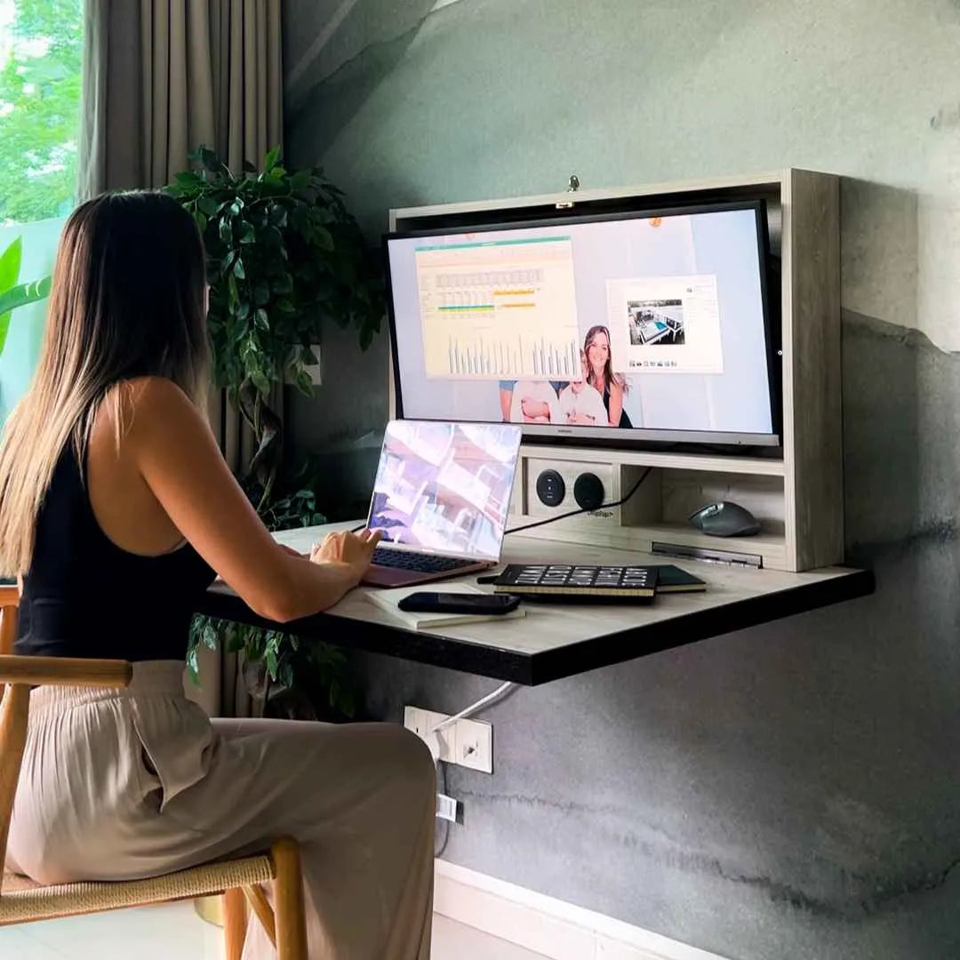 Woman on a video call at an open DropTop desk against a dark textured wall.