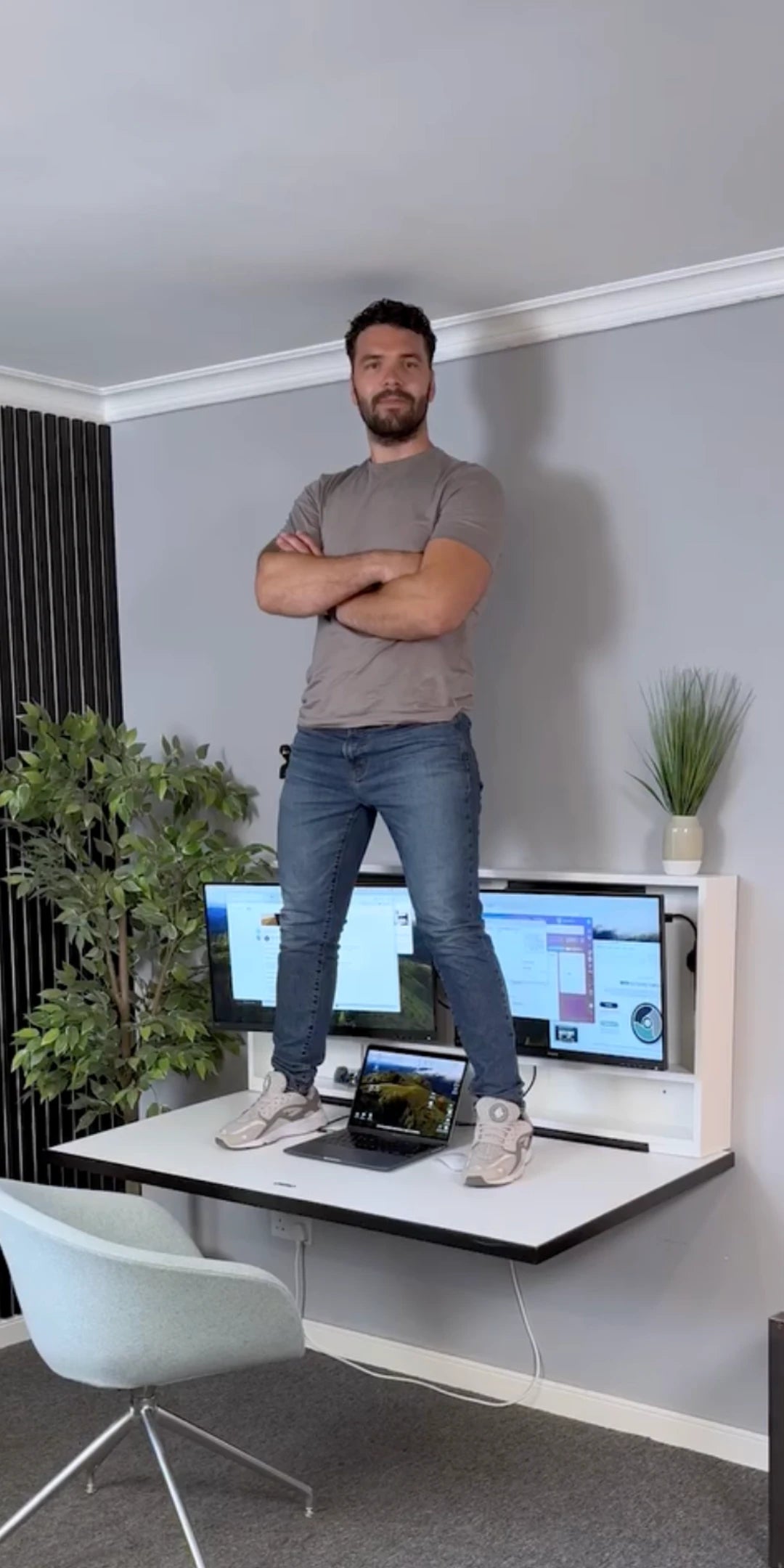 Man standing on an open DropTop desk with two monitors and a laptop, showing how much weight it holds.