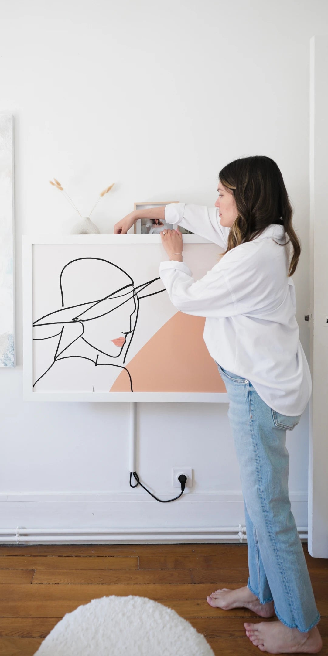 Woman lifting the front of a closed DropTop desk that displays a line-drawing print as wall art.