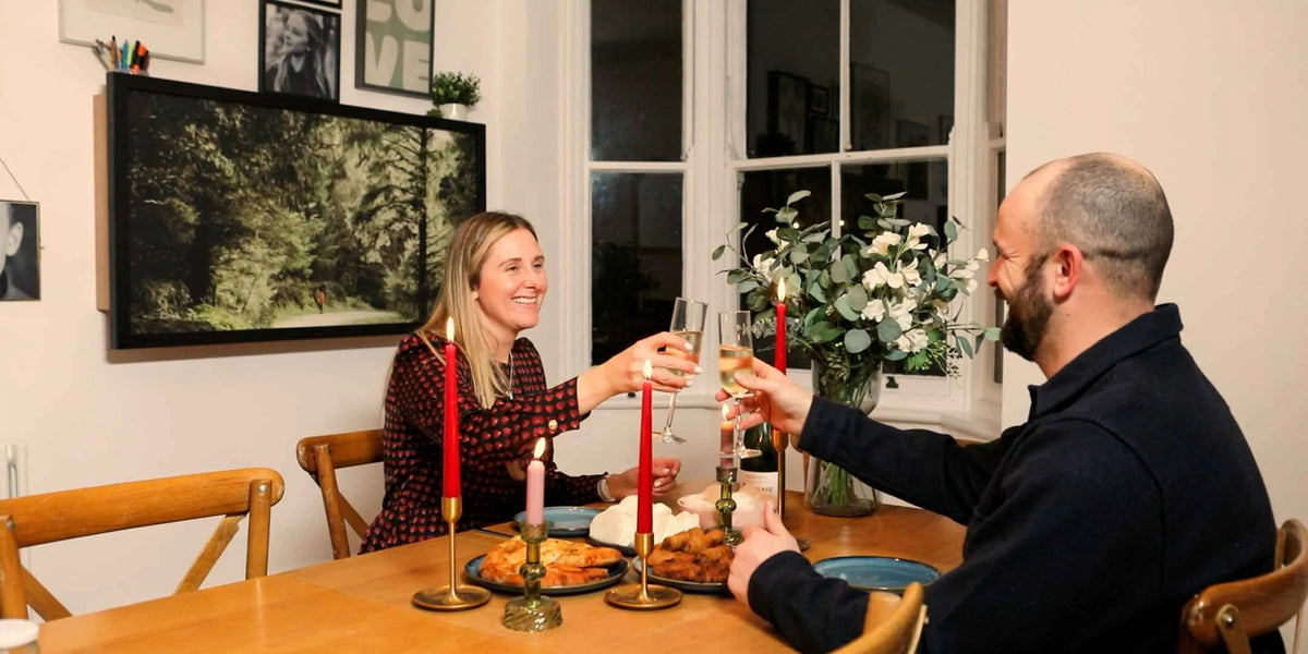 Couple raising a glass at a dinner table with a closed DropTop desk on the wall behind.