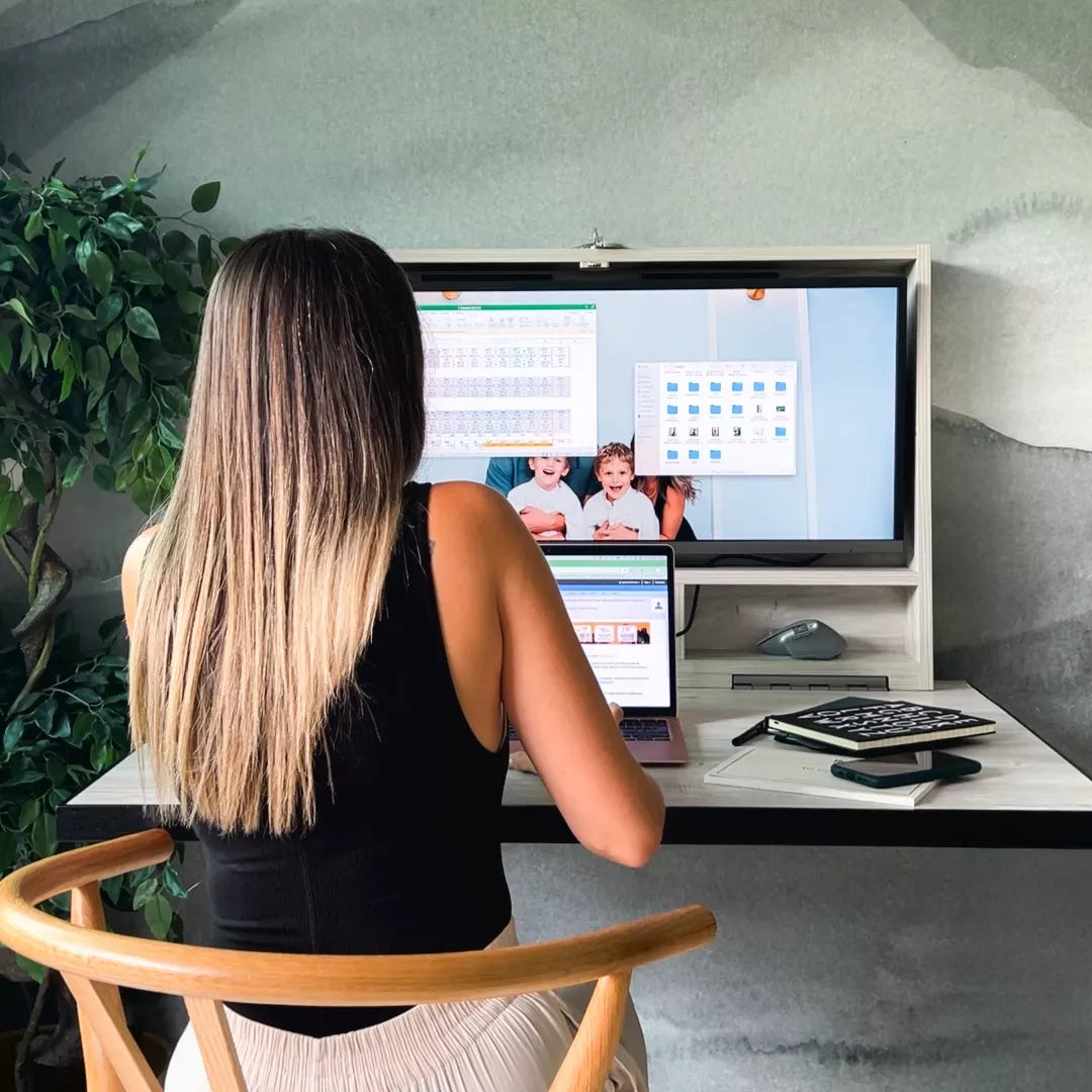 Woman working at an open DropTop desk with a monitor and laptop.