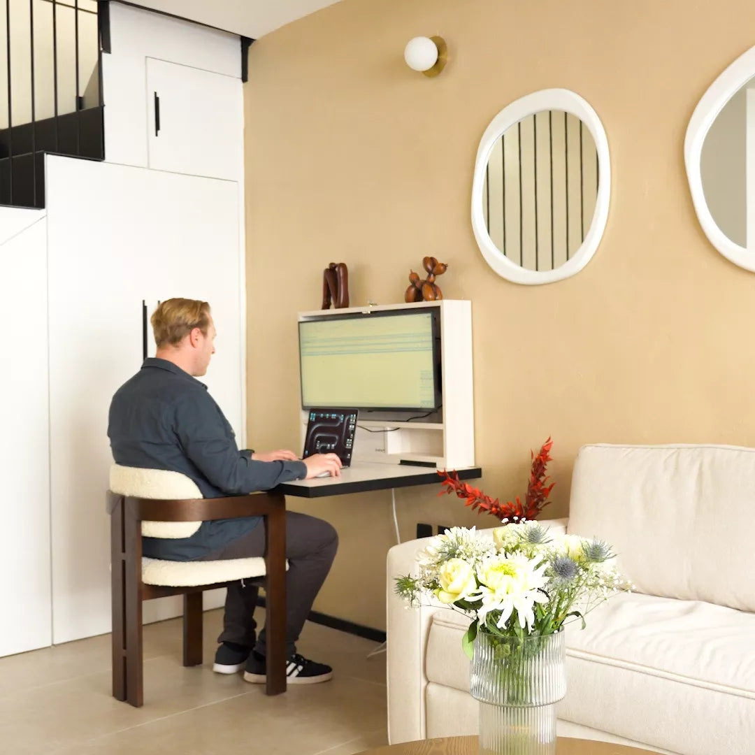 Man working at an open DropTop desk beside a sofa in a living room.