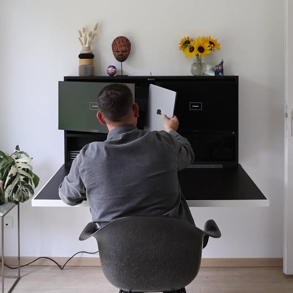 Man sliding a laptop into the storage shelf of a black DropTop desk.
