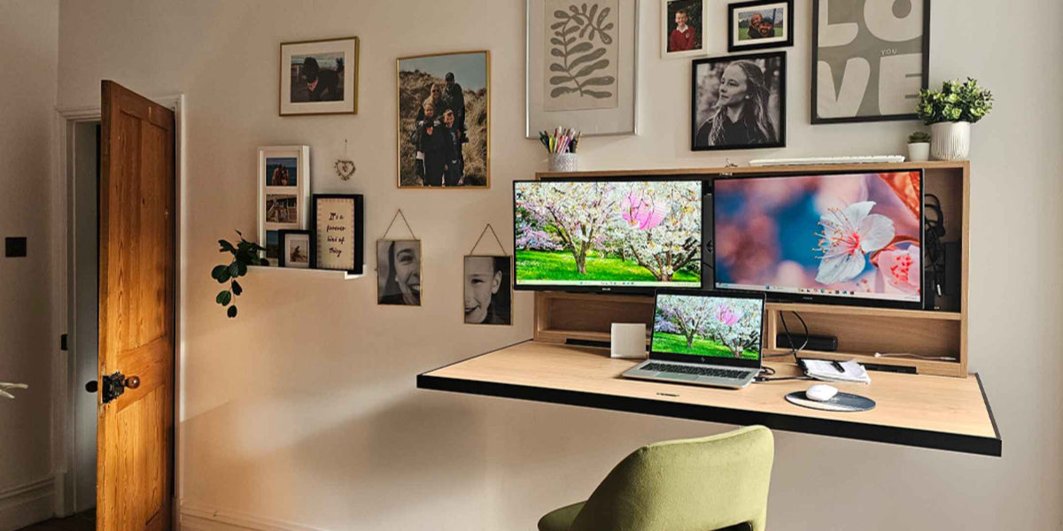 Open DropTop desk with two monitors below a gallery wall of framed pictures.