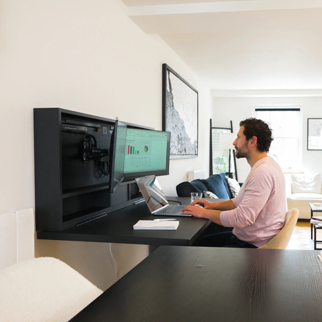 Man working at an open black DropTop desk with a monitor and laptop.