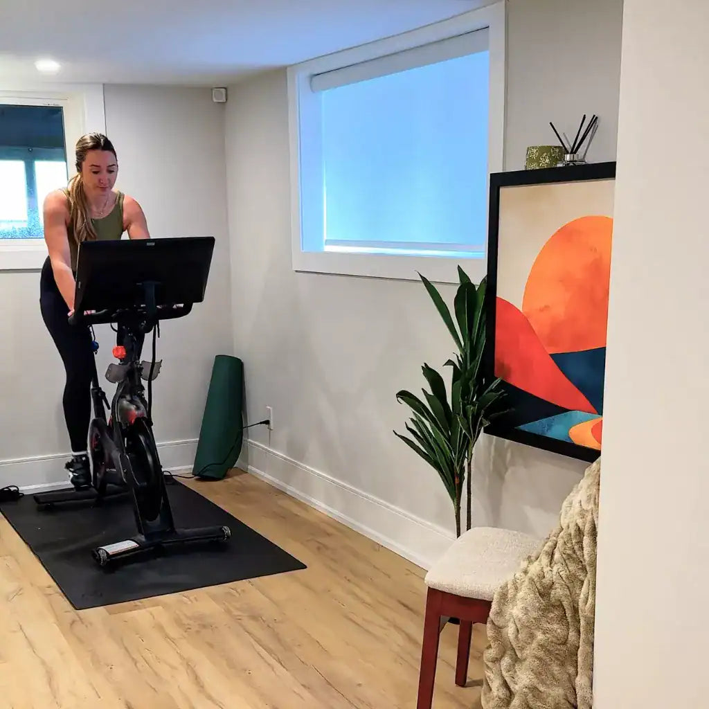 Woman exercising on a spin bike beside a closed DropTop Single 32 showing a sunset print.
