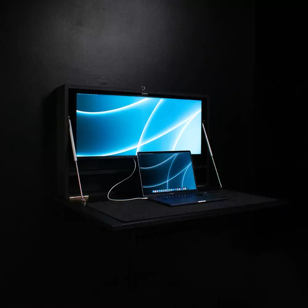 Open black DropTop Single 34 Light against a black wall with a monitor and laptop.