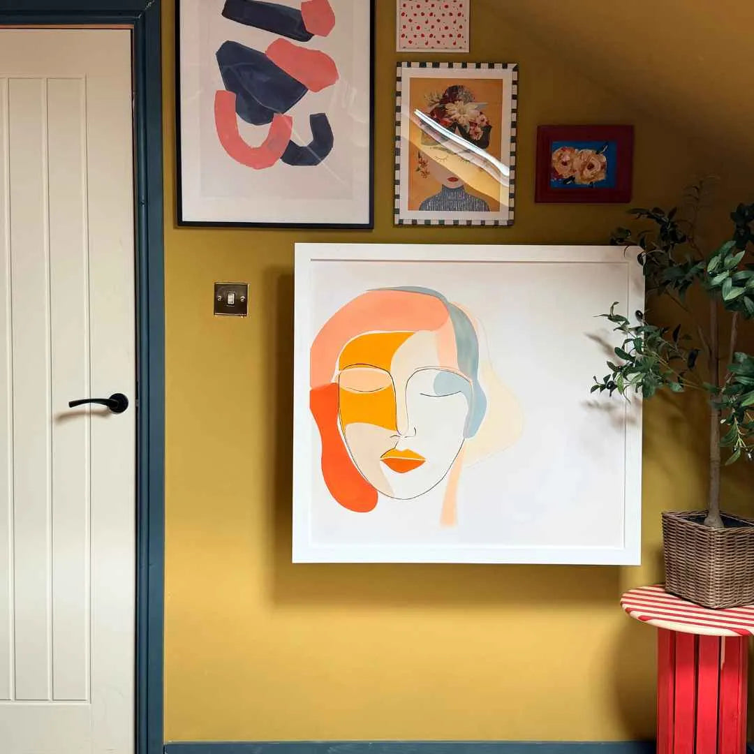 A closed DropTop desk hanging as colorful artwork on a mustard wall, beside a white door and framed prints